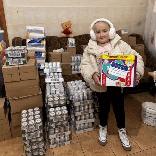 Eleonora stands with donated baby supplies and hygiene products in a humanitarian aid center in Ukraine, helping distribute essential items for families and children affected by the war.