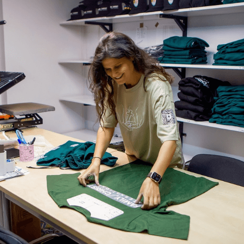 Katya prints ministry shirts at a volunteer workspace in Ukraine, carefully placing a design on green shirts that will be distributed through humanitarian outreach and church ministry efforts.