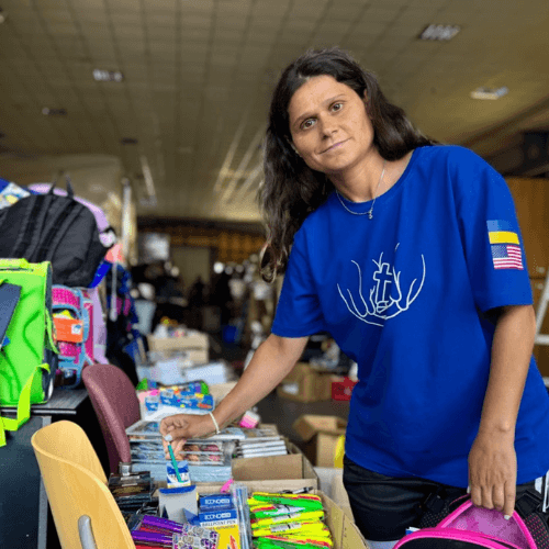 Katya organizes school supplies and donations for children in Ukraine while wearing a ministry shirt with Ukrainian and U.S. flags, helping prepare aid packages for families affected by the war.